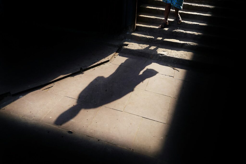A long shadow stretching across sunlit pavement in hard light